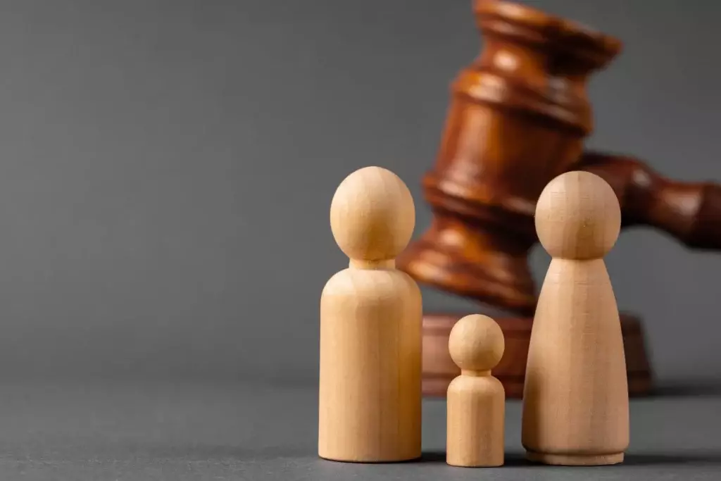 Three wooden figurines of varying sizes stand in front of a Florida judge's gavel on a gray background.
