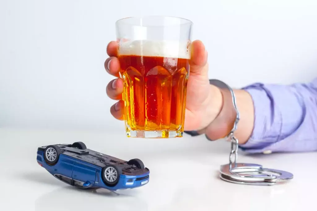 A handcuffed person in Lakeland carefully balances a glass of beer beside a toy car, perhaps pondering their next conversation with an attorney.