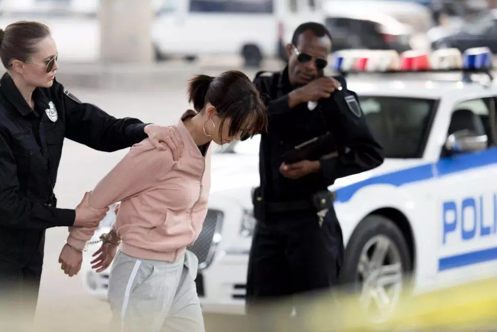 In Florida, police officers are seen arresting a woman in a pink sweatshirt and gray pants near a police car.